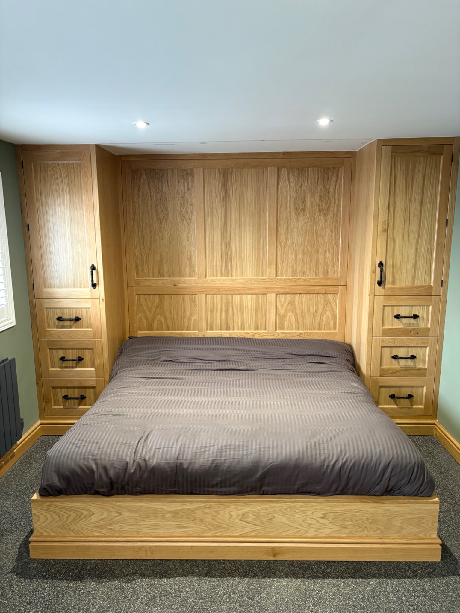 Fitted solid oak wardrobes with shaker doors, a panelled headboard and bed surround in a bedroom in Harwich