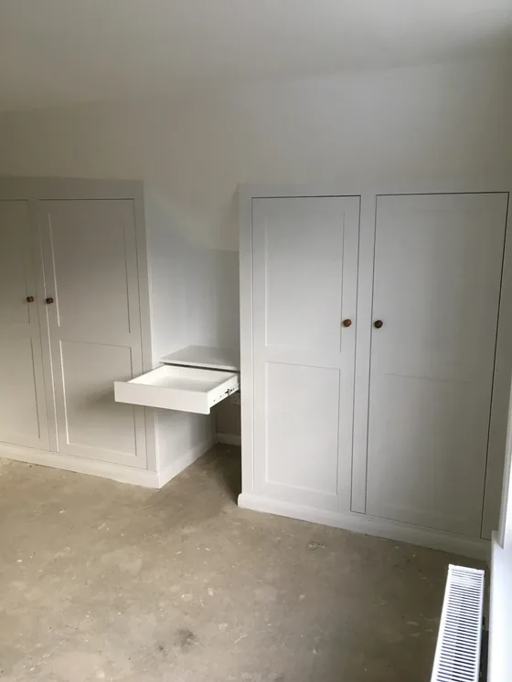 Bespoke fitted wardrobes in a Dedham bedroom cut into a sloping ceiling with a pull-out shelf